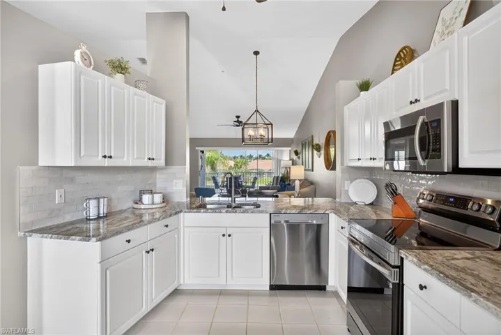 Kitchen featuring stainless steel appliances, a ceiling fan, vaulted ceiling, white cabinets, and light tile patterned floors