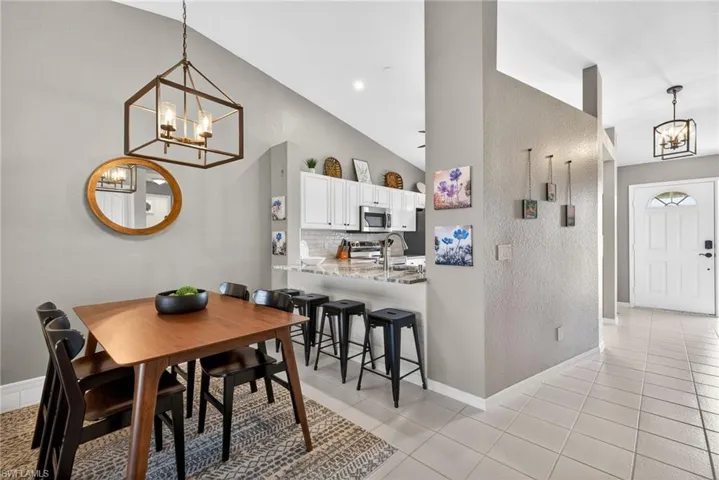 Dining area featuring a chandelier, a textured wall, light tile patterned floors, and vaulted ceiling