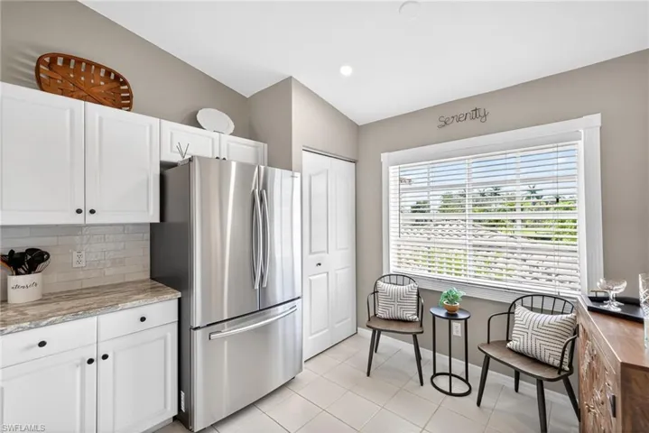 Kitchen featuring freestanding refrigerator, white cabinets, light stone counters, vaulted ceiling, and light tile patterned floors