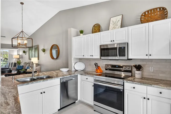 Kitchen featuring stainless steel appliances, light stone counters, white cabinets, vaulted ceiling, and hanging lights