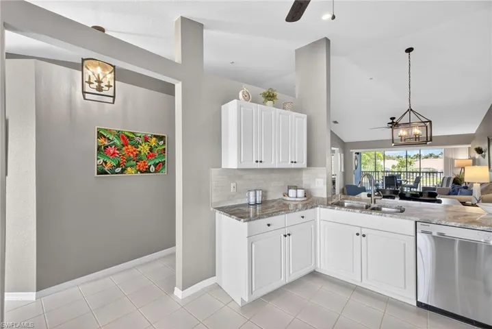 Kitchen featuring hanging lights, ceiling fan, open floor plan, stainless steel dishwasher, and dark stone countertops