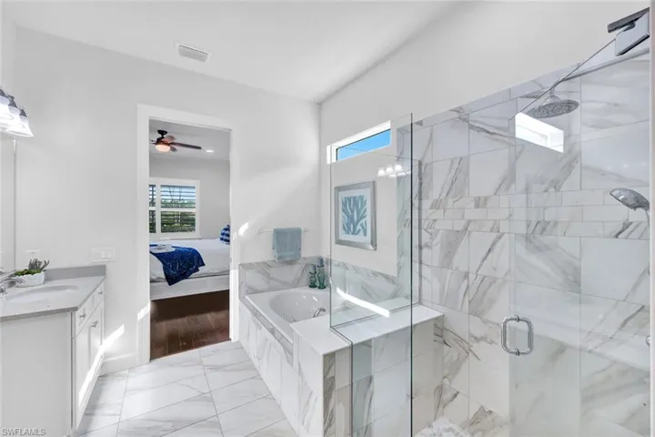 Primary bathroom with tile floors, dual sinks, tub and glass enclosed tiled shower.