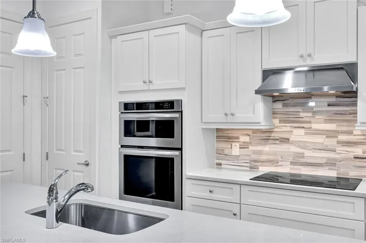 Kitchen with quartz countertops, white wood cabinetry, tile backsplash, cooktop and stainless steel appliances.
