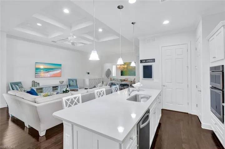 Kitchen with quartz countertops, white wood cabinetry, stainless steel appliances, hardwood floors, pantry (with access to the laundry room at the right).