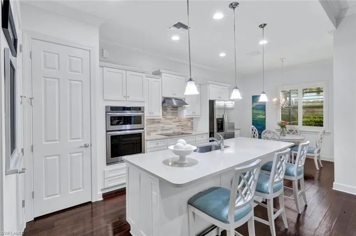 Kitchen with quartz countertops, white wood cabinetry, stainless steel appliances, hardwood floors, breakfast nook and pantry (with access to the laundry room at the far left - not shown).