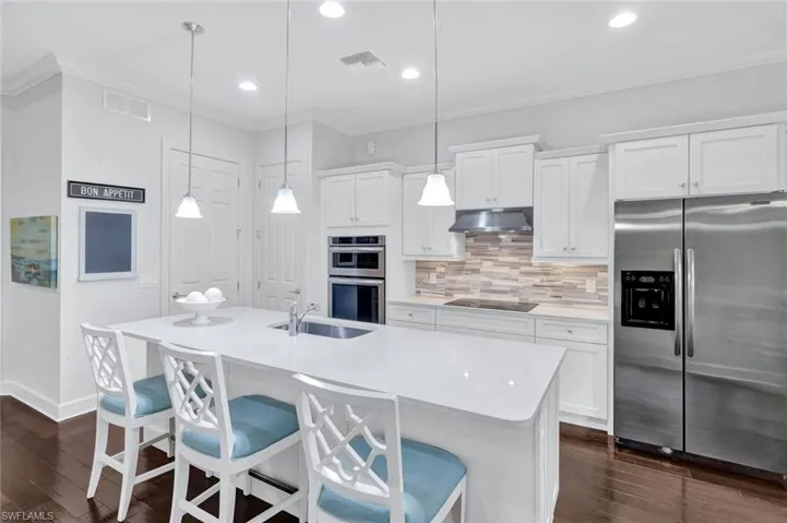 Kitchen with quartz countertops, white wood cabinetry, tile backsplash, cooktop and stainless steel appliances.