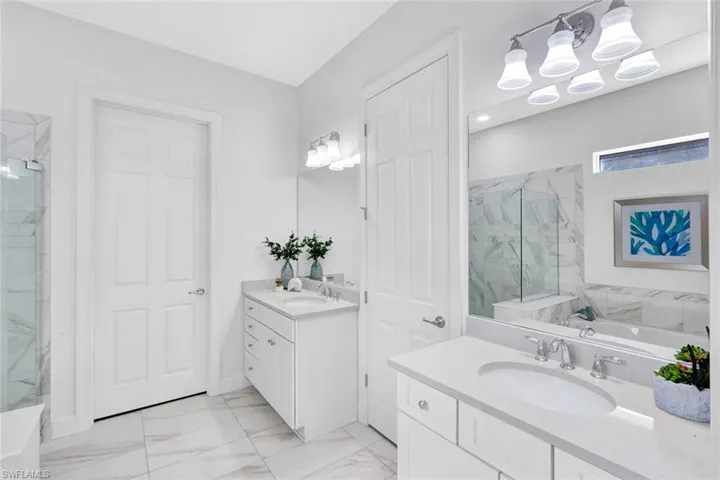 Primary bathroom with tile floors, dual sinks, tub and glass enclosed tiled shower and door to the master closet (to the left) and door to the W/C (to the right).