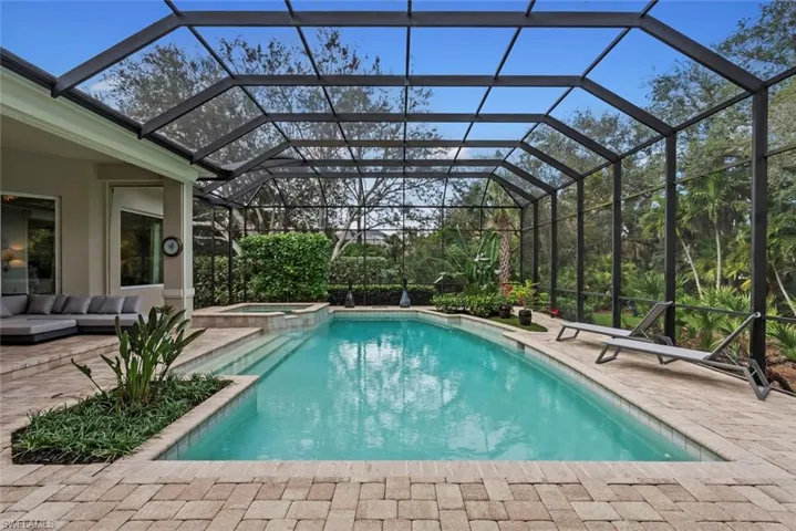 View of swimming pool featuring a patio, a pool with connected hot tub, and glass enclosure