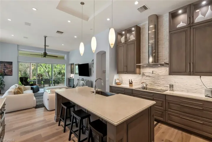 Kitchen featuring a sink, wall chimney range hood, open floor plan, black electric stovetop, and recessed lighting