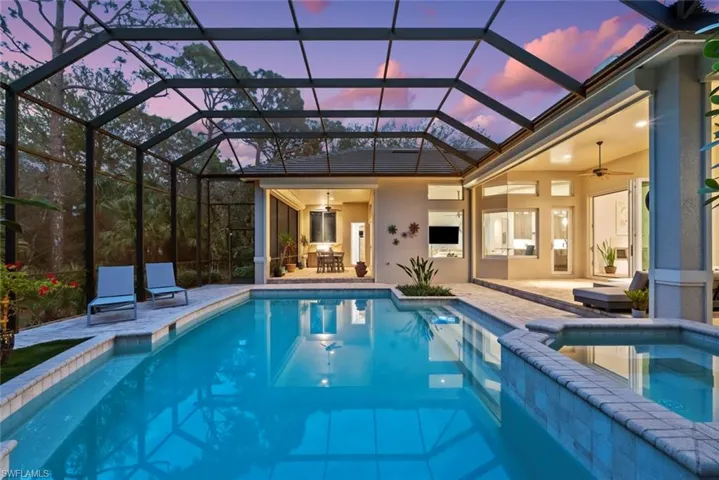 Pool at dusk featuring a ceiling fan, a patio, a pool with connected hot tub, and glass enclosure