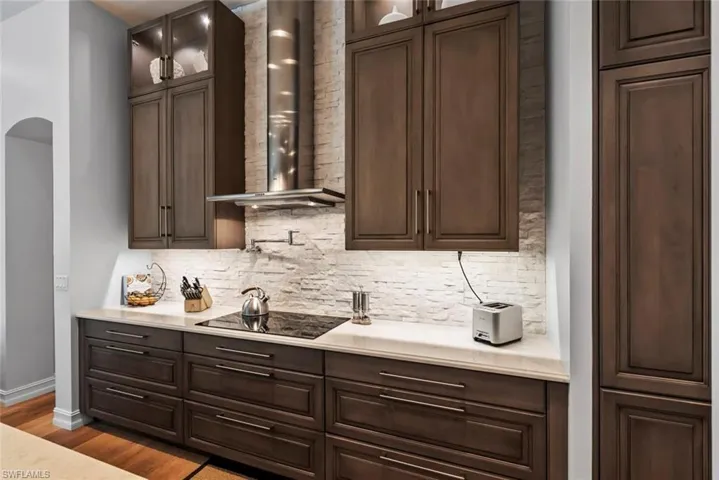 Bar featuring black electric cooktop, wall chimney exhaust hood, decorative backsplash, and arched walkways