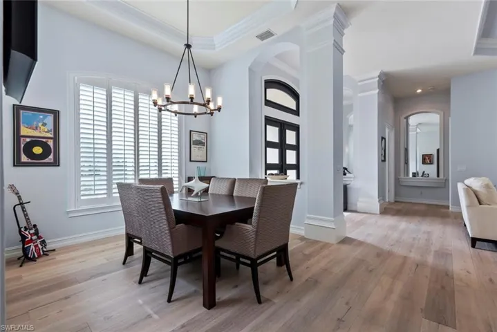 Dining room with arched walkways, ornamental molding, a chandelier, light wood-style flooring, and decorative columns