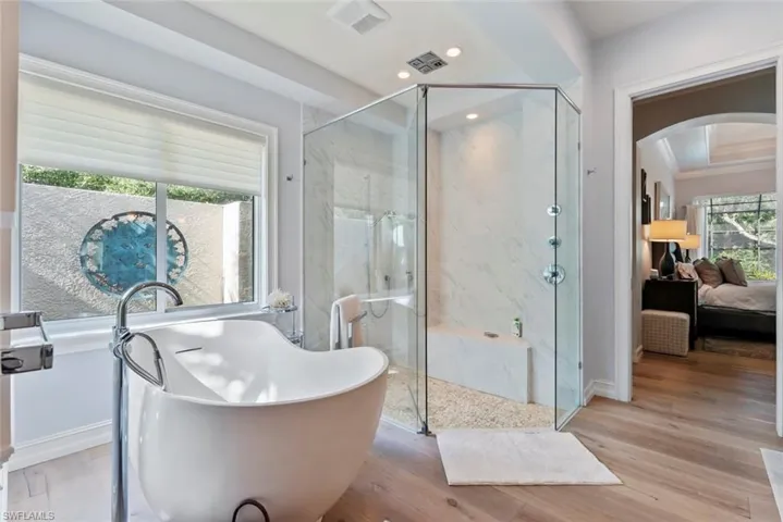 Ensuite bathroom featuring a marble finish shower, a freestanding bath, wood finished floors, baseboards, and recessed lighting