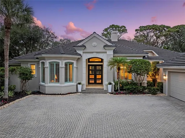 French provincial home featuring decorative driveway, a tiled roof, stucco siding, and a chimney