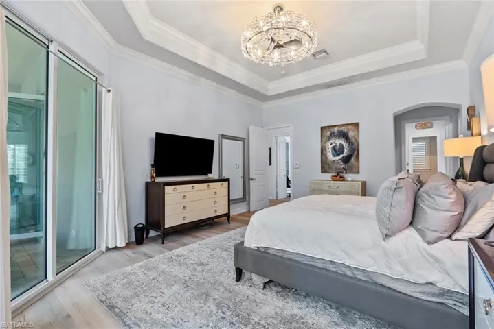 Bedroom with a tray ceiling, wood finished floors, a chandelier, arched walkways, and ornamental molding