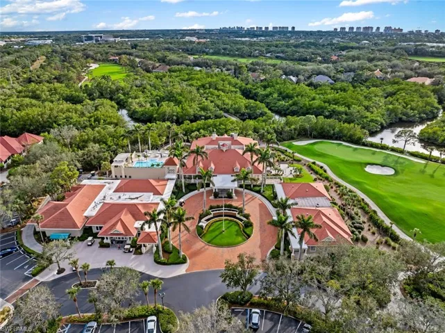 Drone / aerial view of a golf club, skyline, a tree filled landscape, and a large body of water