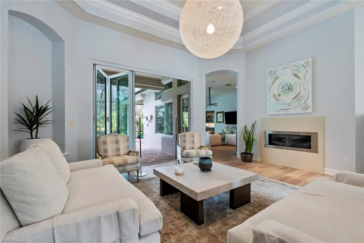 Living room with arched walkways, wood finished floors, crown molding, a glass covered fireplace, and baseboards