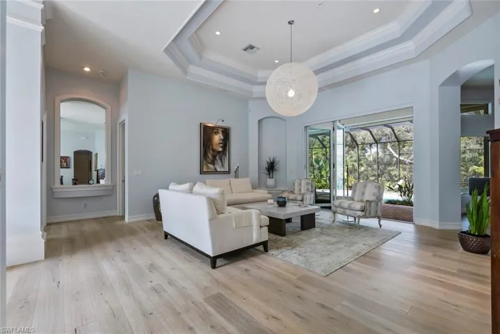 Living area featuring arched walkways, a tray ceiling, crown molding, light wood-style floors, and baseboards