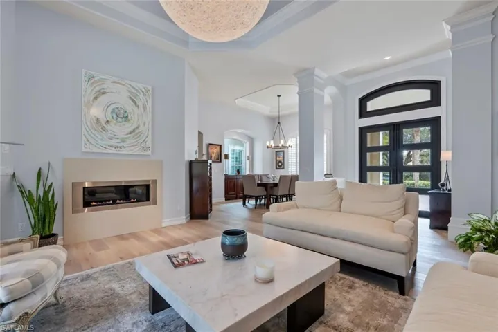 Living room with arched walkways, healthy amount of natural light, light wood-style flooring, ornamental molding, and a glass covered fireplace