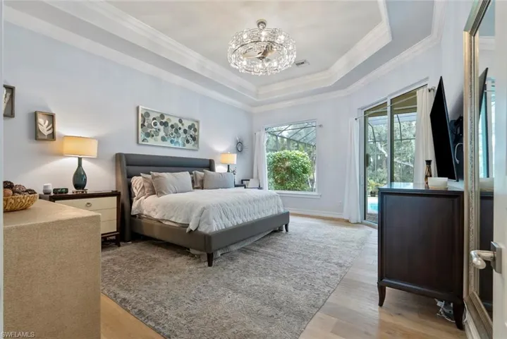 Bedroom with ornamental molding, a chandelier, wood finished floors, access to outside, and a raised ceiling
