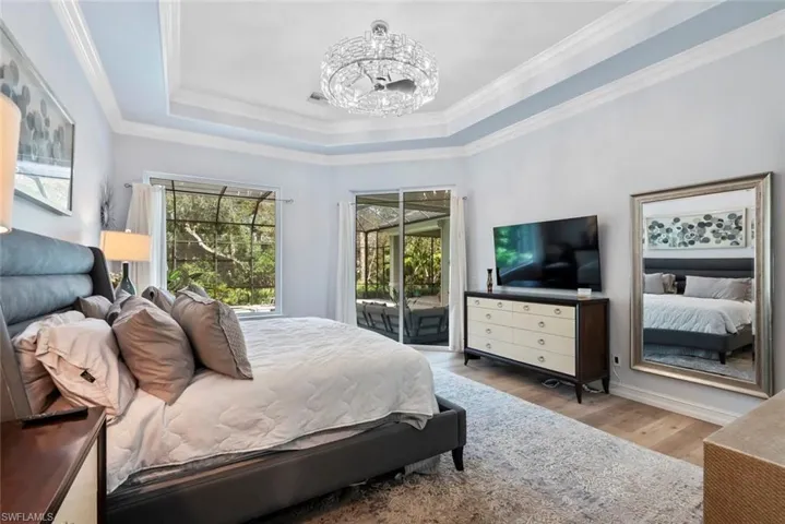 Bedroom featuring a chandelier, access to outside, wood finished floors, a tray ceiling, and crown molding