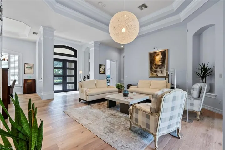 Living area featuring a raised ceiling, decorative columns, light wood-type flooring, crown molding, and a high ceiling