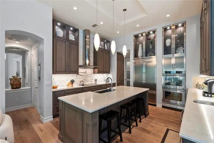 Kitchen featuring a sink, wall chimney exhaust hood, appliances with stainless steel finishes, light wood-style flooring, and tasteful backsplash