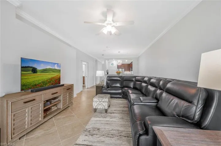 Living room featuring crown molding, light tile patterned flooring, and ceiling fan