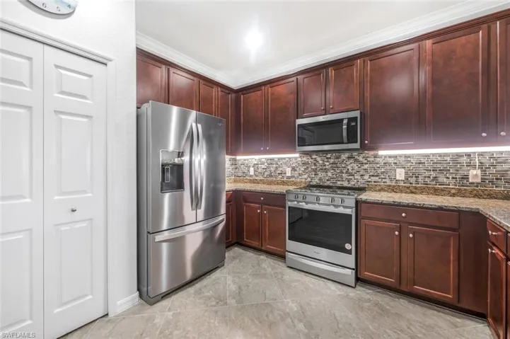 Kitchen featuring crown molding, dark stone counters, decorative backsplash, light tile patterned floors, and appliances with stainless steel finishes