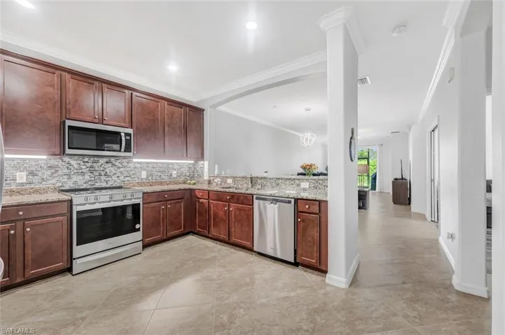 Kitchen featuring backsplash, crown molding, light stone countertops, and appliances with stainless steel finishes