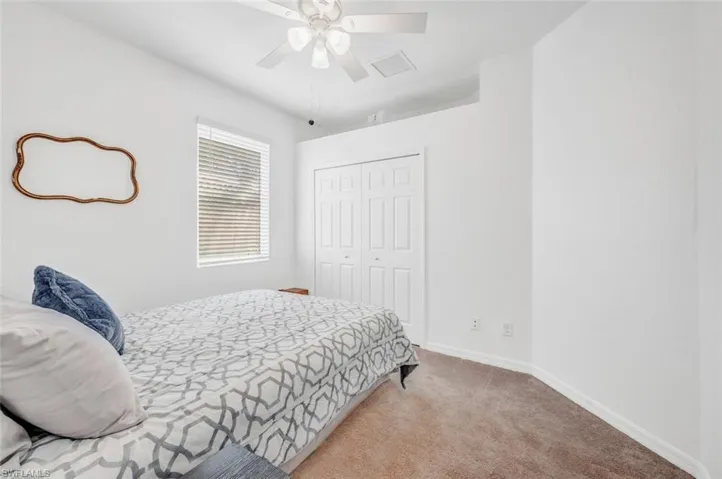 Carpeted bedroom with ceiling fan and a closet