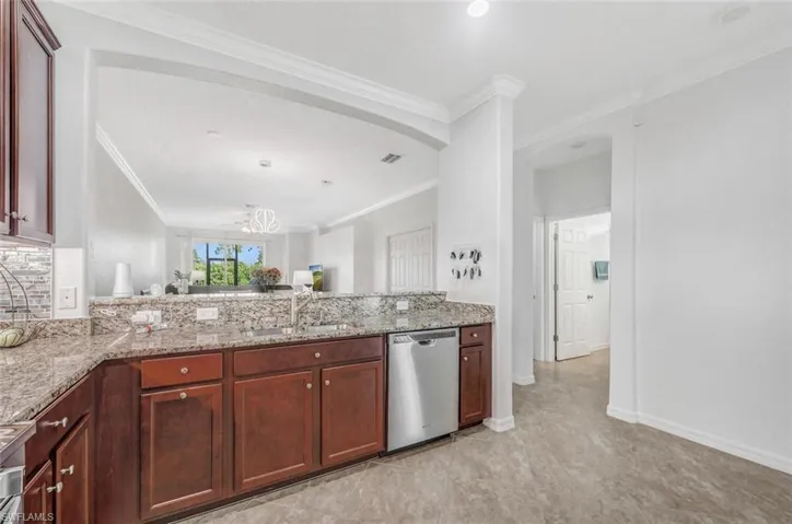 Kitchen featuring stainless steel dishwasher, light stone counters, sink, and a chandelier