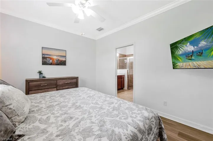 Bedroom featuring ensuite bath, ceiling fan, light hardwood / wood-style floors, and ornamental molding