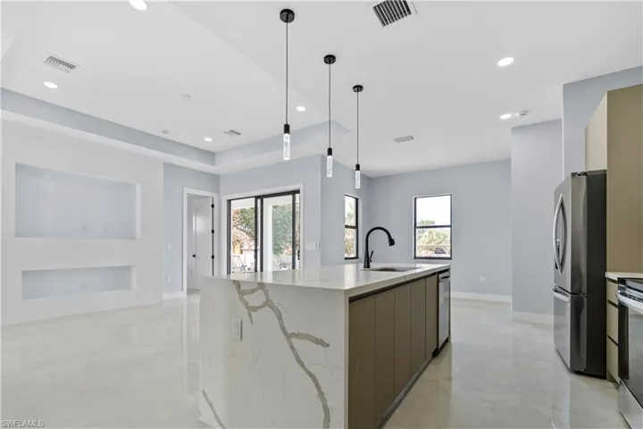 Kitchen featuring light stone counters, an island with sink, stainless steel appliances, and plenty of natural light
