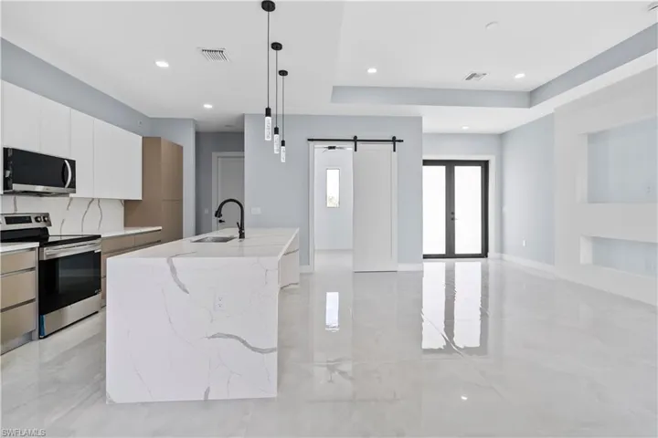 Dual tone kitchen with stainless steel appliances, light stone counters, a barn door, dual tone cabinetry, and hanging light fixtures