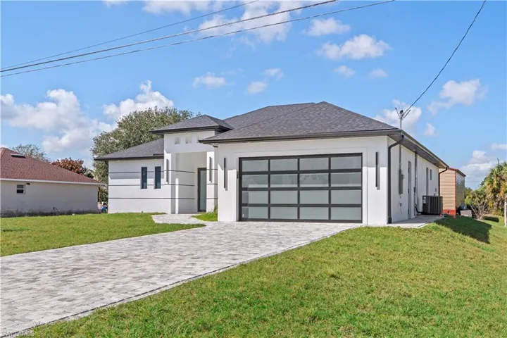 View of front of property with a front yard, decorative driveway, stucco siding, and roof with shingles