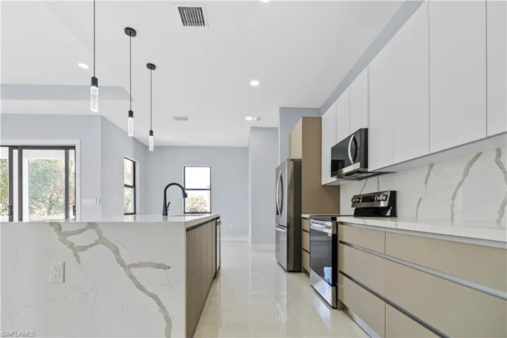Two tone kitchen featuring stainless steel appliances, two tone cabinetry, light stone countertops, hanging light fixtures, and modern cabinets