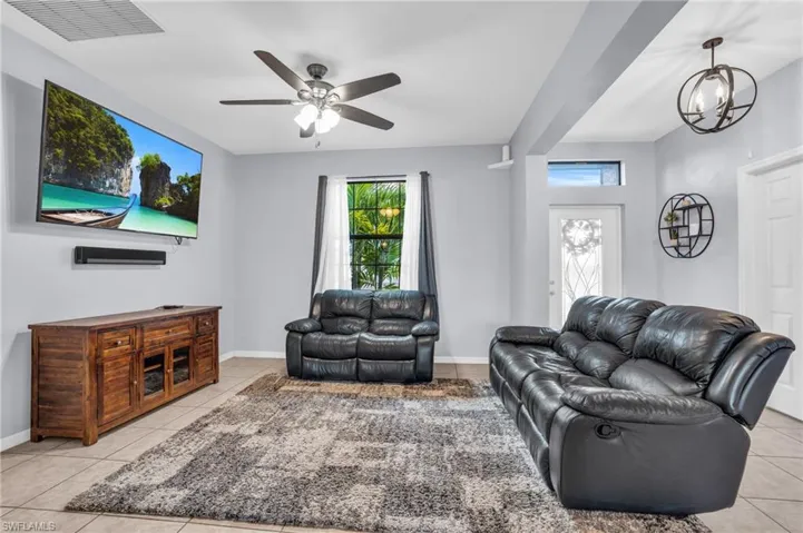 Living room featuring ceiling fan with notable chandelier and light tile flooring