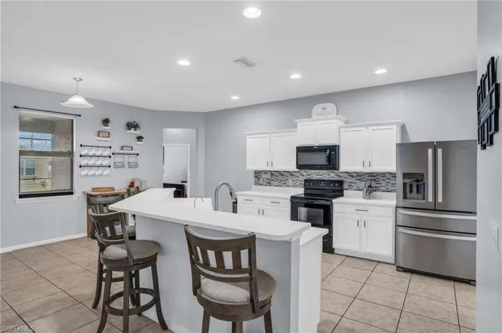 Kitchen with decorative light fixtures, light tile flooring, black appliances, backsplash, and white cabinetry