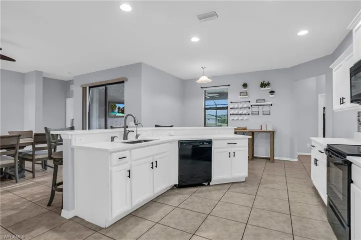 Kitchen with black appliances, sink, light tile floors, and hanging light fixtures