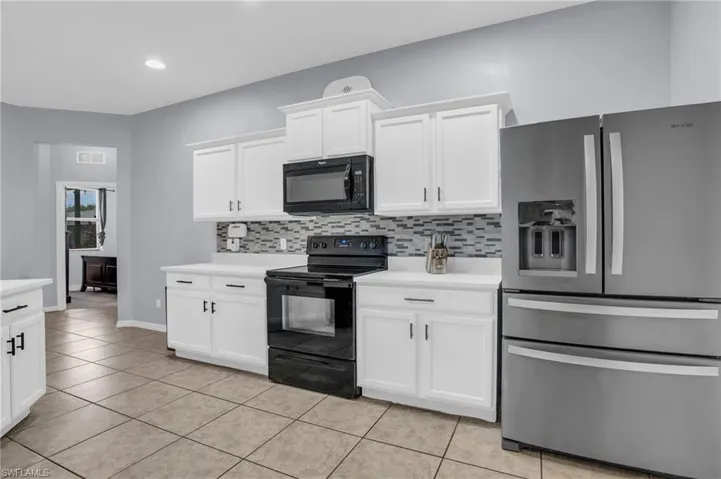 Kitchen with white cabinetry, backsplash, black appliances, and light tile floors