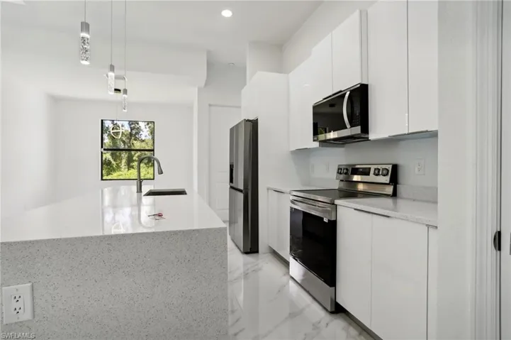 Kitchen with white cabinetry, hanging light fixtures, stainless steel appliances, a kitchen island with sink, and sink