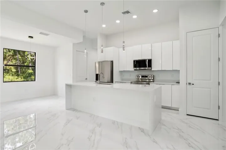Kitchen featuring hanging light fixtures, an island with sink, stainless steel appliances, and light tile flooring