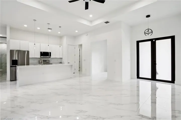 Kitchen with a center island with sink, stainless steel appliances, decorative light fixtures, ceiling fan, and light tile floors