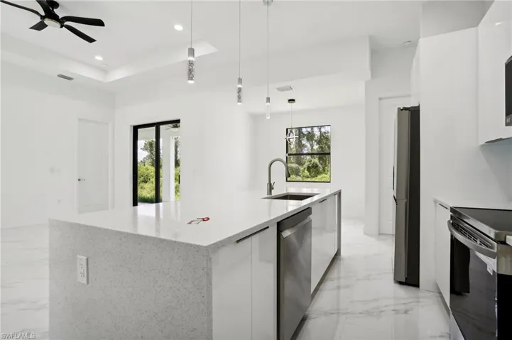 Kitchen featuring light tile flooring, a raised ceiling, hanging light fixtures, sink, and white cabinets