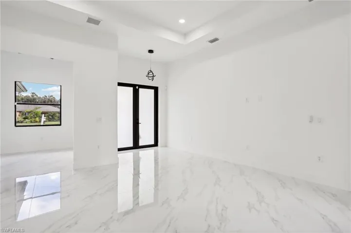 Tiled empty room featuring a tray ceiling and french doors