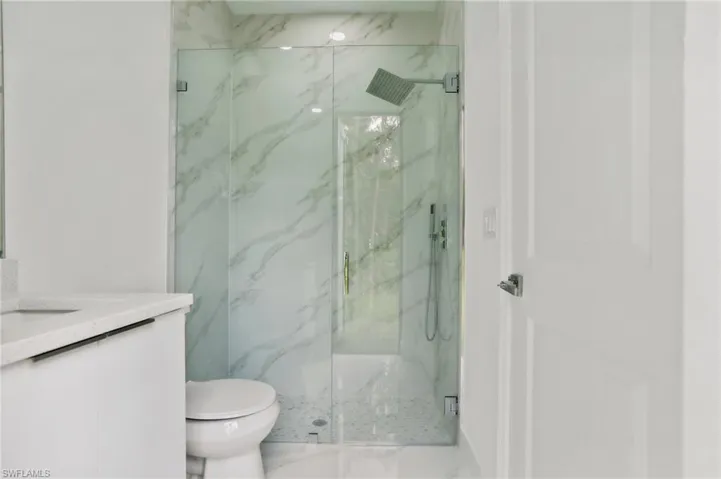 Bathroom with a shower with shower door, vanity, and toilet