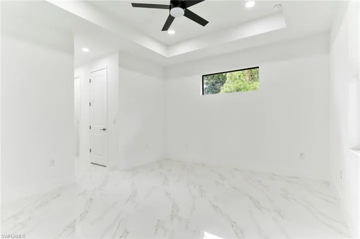 Spare room with ceiling fan, a raised ceiling, and light tile floors