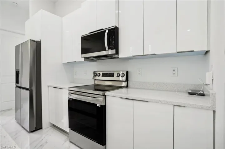Kitchen with appliances with stainless steel finishes, light stone counters, white cabinets, and light tile floors