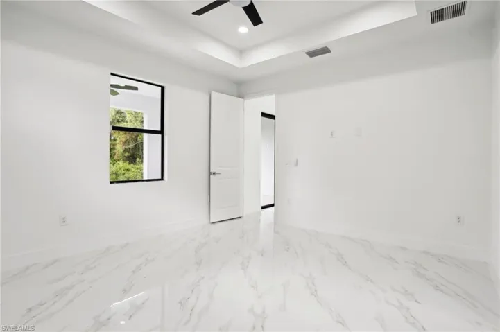 Empty room featuring a raised ceiling, ceiling fan, and light tile floors